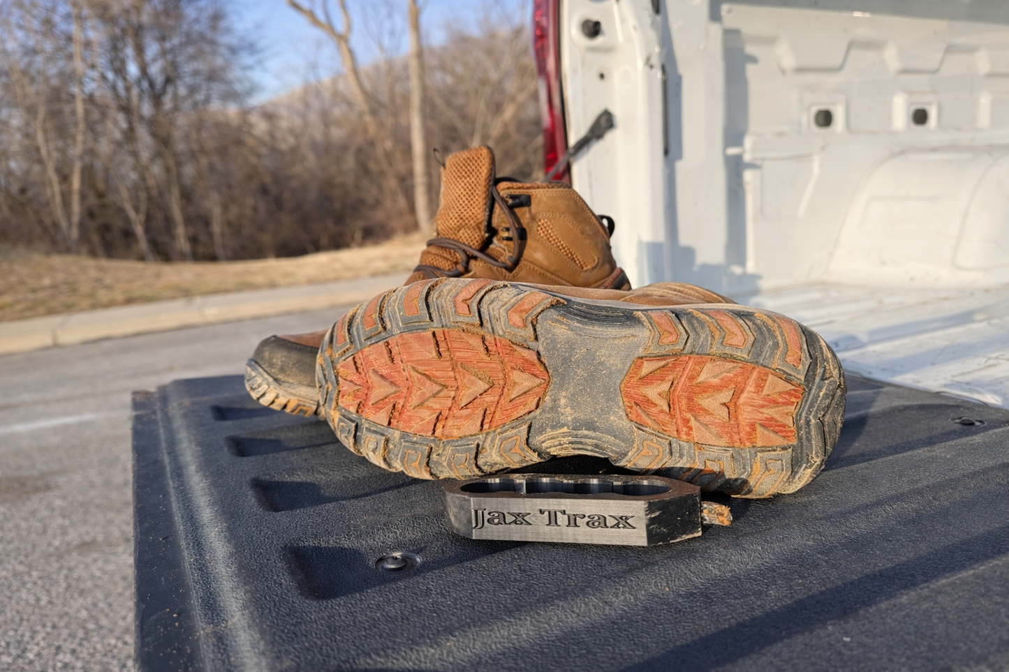 Work boots resting on the tailgate of a truck, with a black boot-cleaning tool labeled “Jax Trax” placed beneath the sole of one boot.