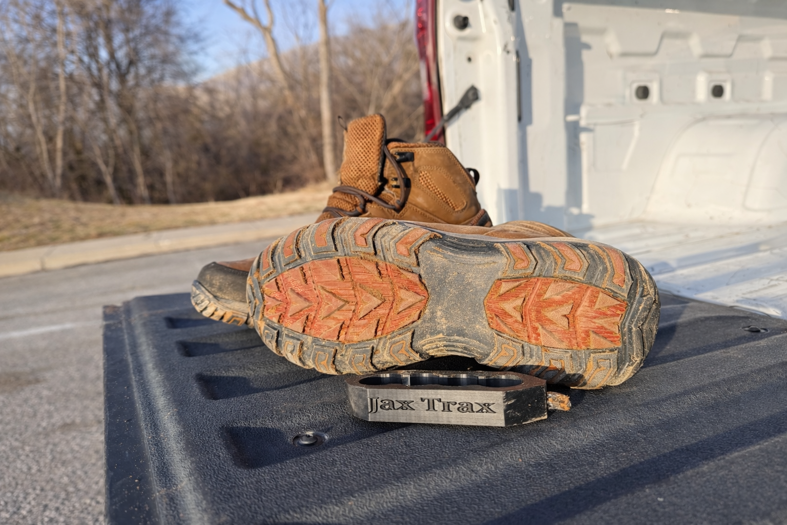 Work boots resting on the tailgate of a truck, with a black boot-cleaning tool labeled “Jax Trax” placed beneath the sole of one boot.